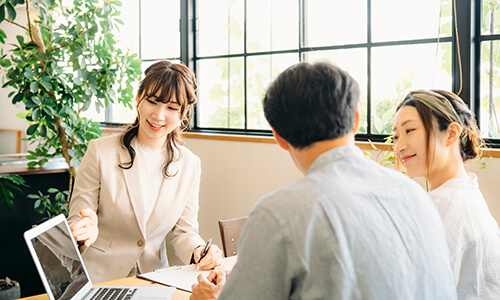 ビジネススーツを着た女性がお客様を相手に右手を差し出し説明している様子のイメージ画像